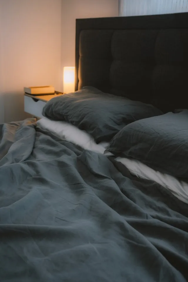 Bed with dark bedding lit by a warm bedside lamp