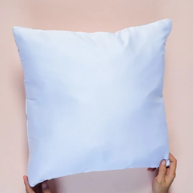 Hands holding up a plain white pillow against a pink background