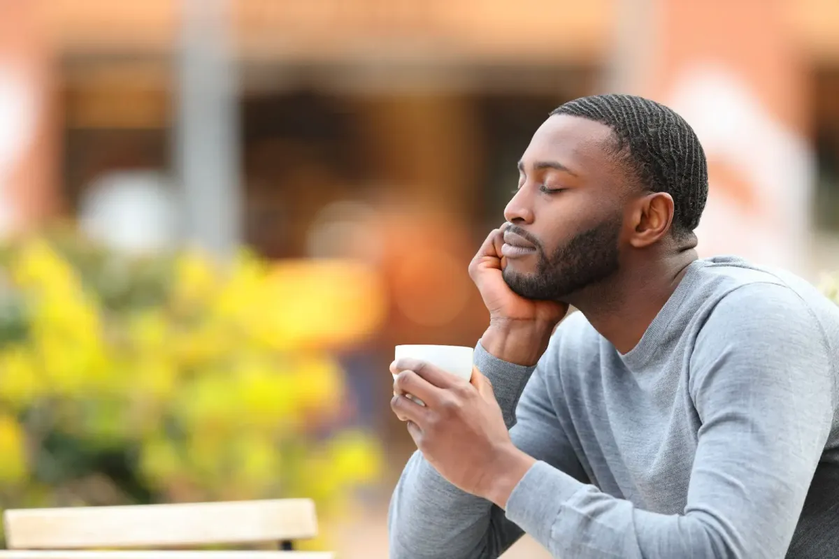 Man sitting outdoors with his eyes closed, relaxing with a cup of coffee